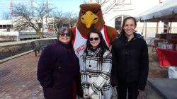 Three people standing with Rocky the Red Hawk