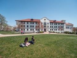 exterior shot of Russ Hall on a sunny day with a few students in the quad