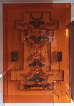 一件由电路板和电线制成的艺术品贴在墙上，后面是橙色的丙烯酸树脂.