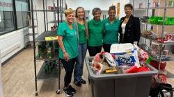 五名女性志愿者站在食品储藏室，拿着装满捐赠物资的箱子.