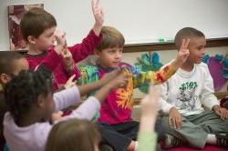 孩子们坐在教室的地板上，举起手臂.