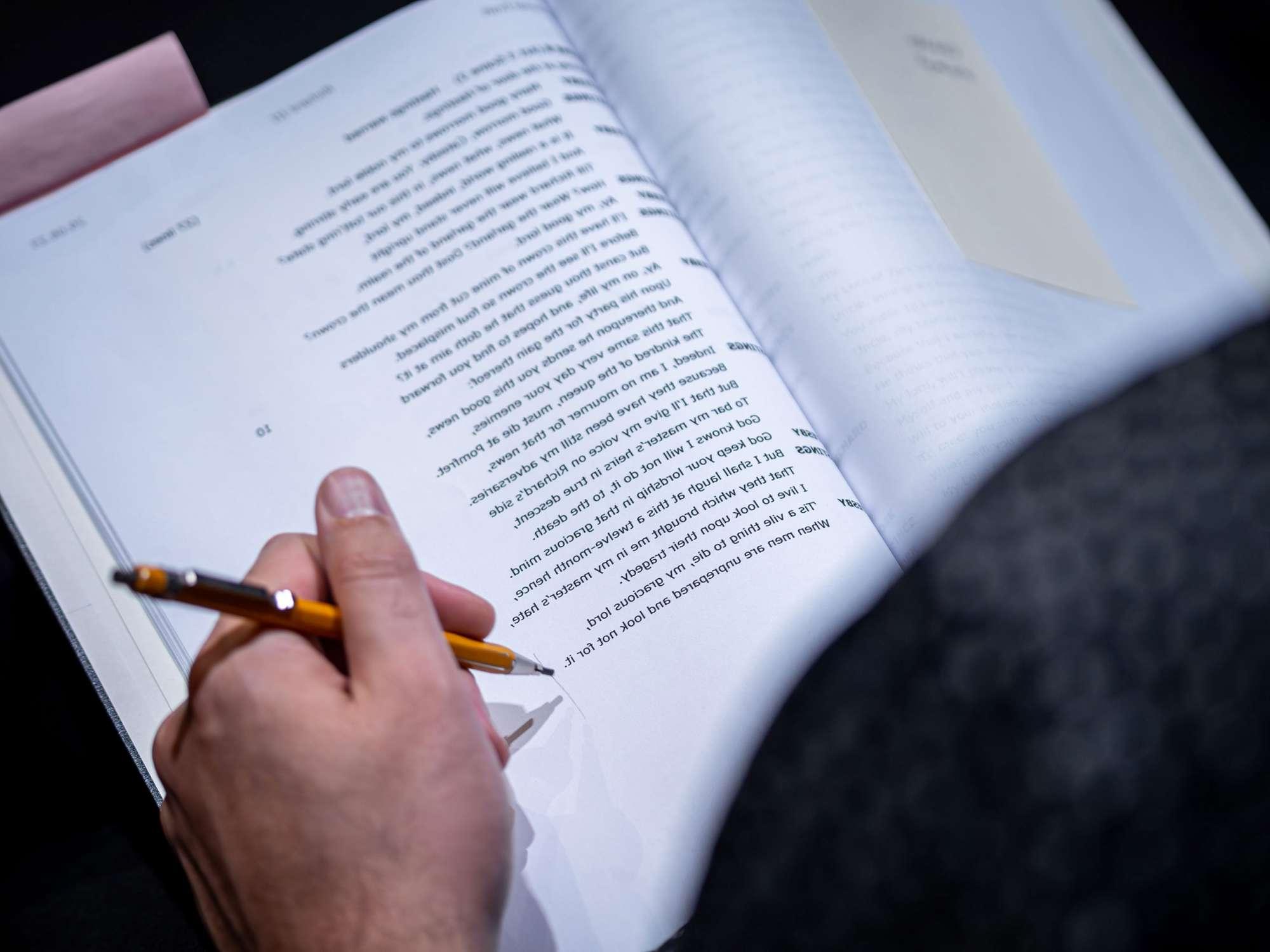 一只手拿着铅笔，顺着莎士比亚剧本的一页写着.