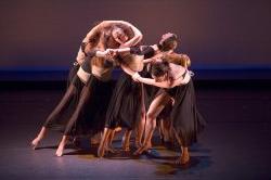 Photo of dancers in tight group, arms interlocked.